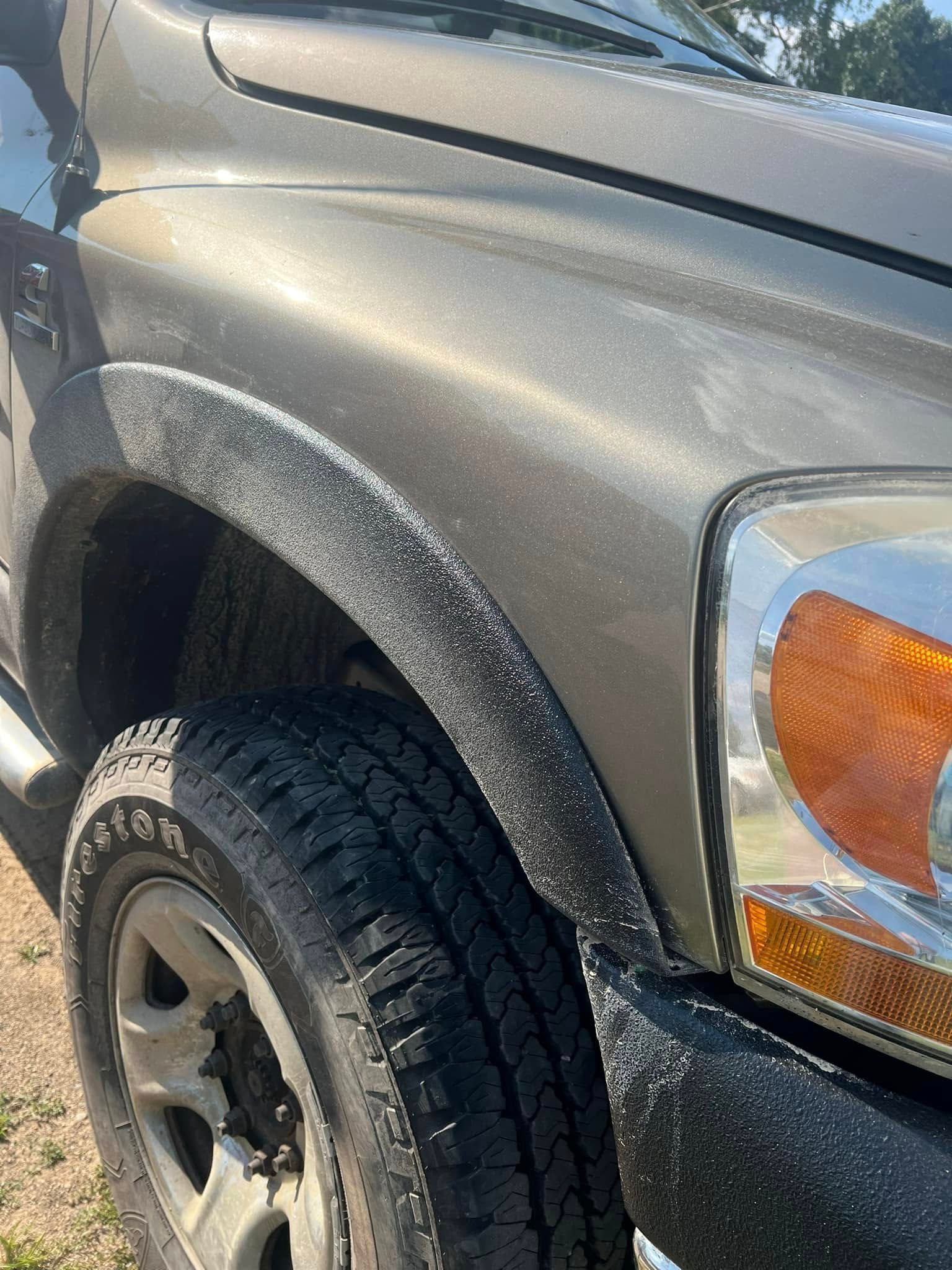 Close-up of a gray pickup truck’s front fender and tire, with the amber headlight visible.