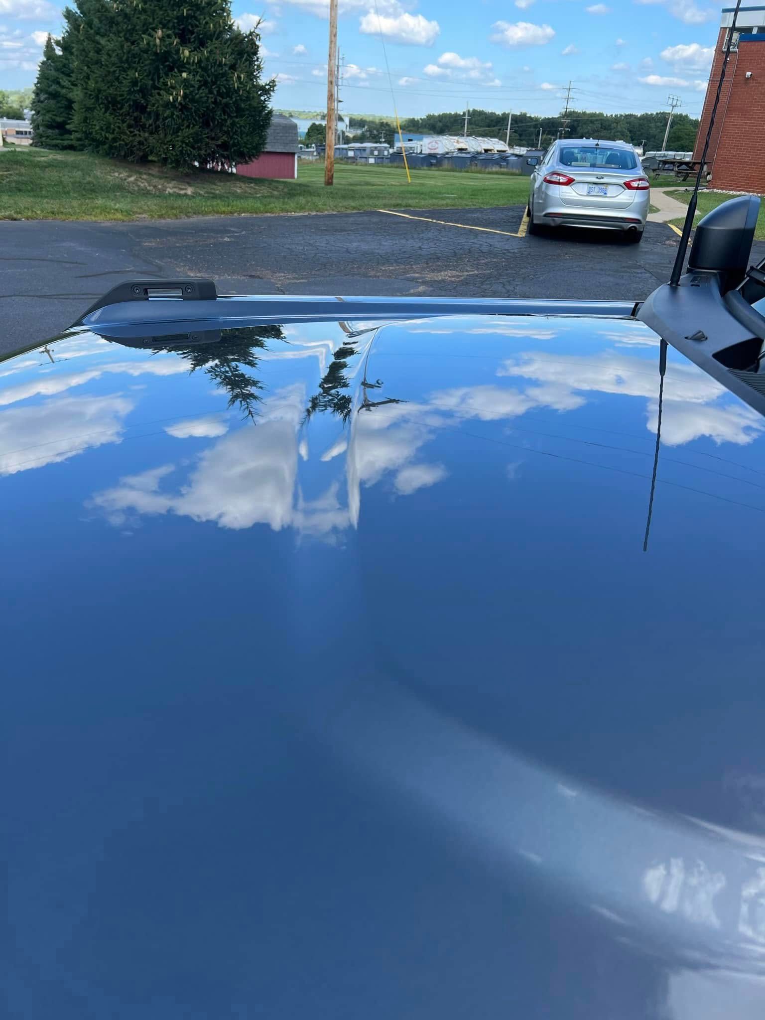 Blue car hood reflecting clouds and a driveway with parked cars ahead