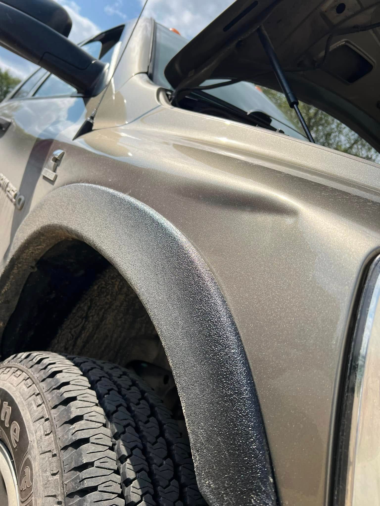 Close-up of a silver SUV’s front fender and tire with speckled paint damage above the wheel.