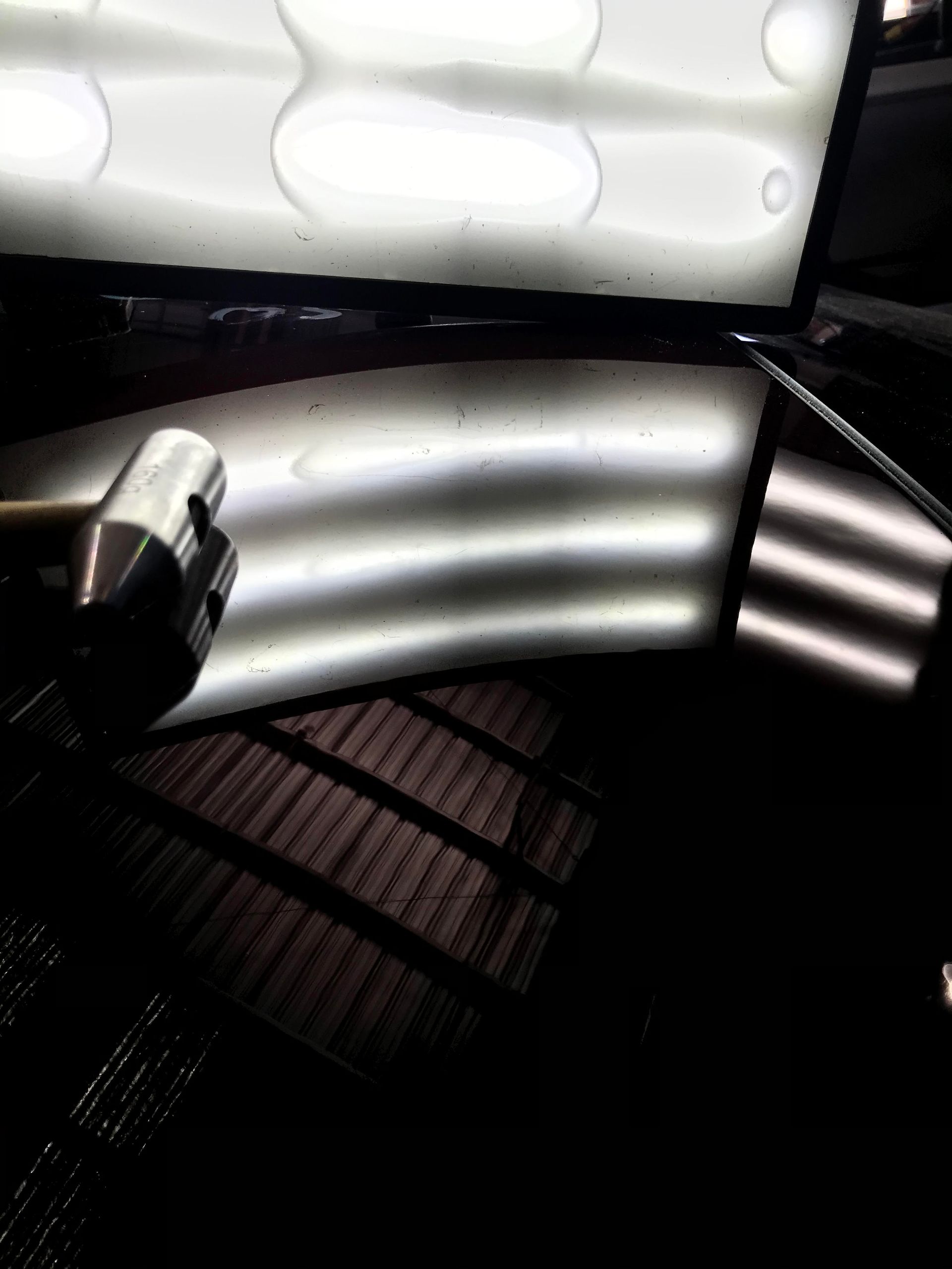 Curved illuminated ceiling panels reflecting on a glossy dark surface with a metal fixture in the corner
