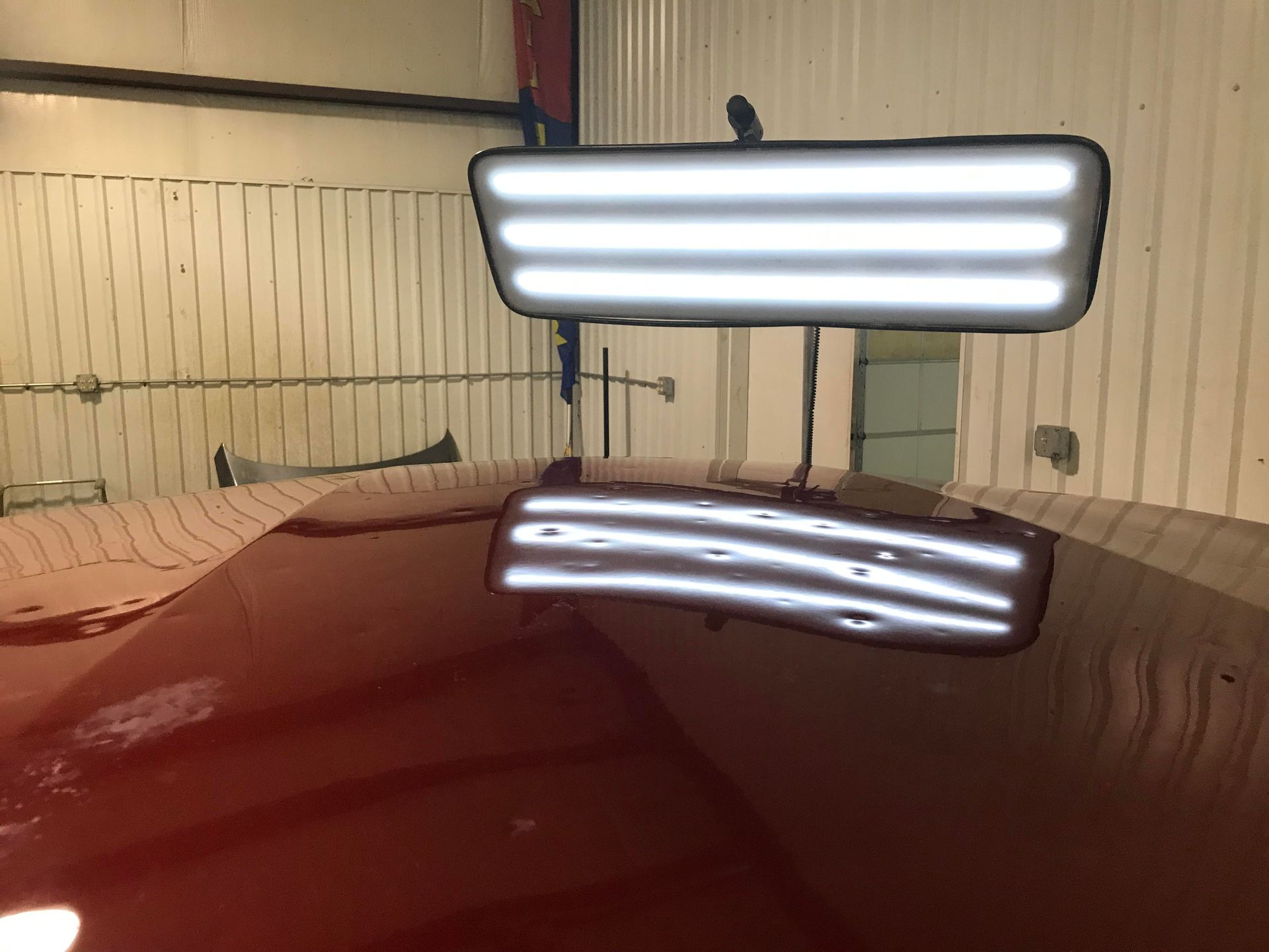 Garage scene with a glossy red car hood reflecting a bright overhead light and garage door.