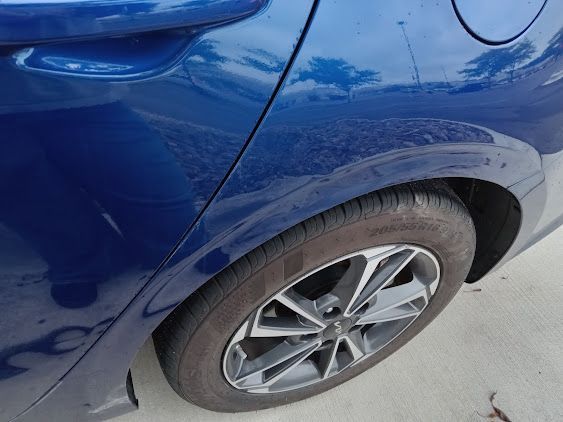 Blue car rear wheel with a dented fender and scuffed body panel