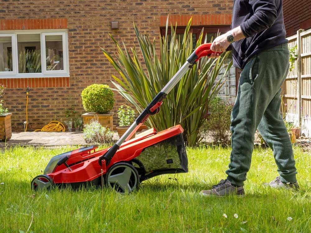 A Man is Mowing His Lawn With a Red Lawn Mower — Great Lakes Mowers & Chainsaws In Pacific Palms, NSW