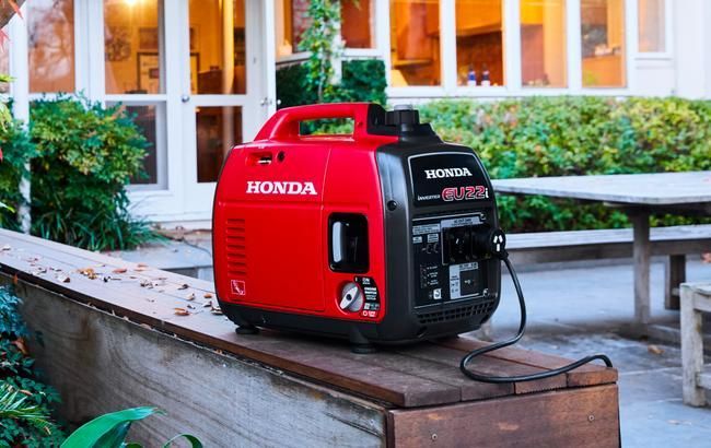 Red Honda portable generator on a wooden deck beside a picnic table outdoors