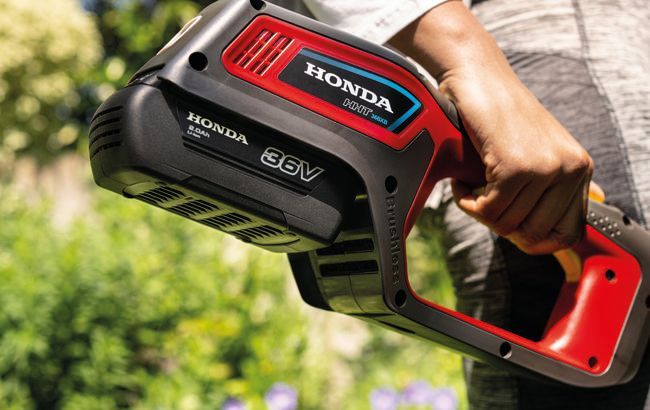 Hand Holding a Red-and-black Honda 56v Battery Pack — Great Lakes Mowers & Chainsaws In Tuncurry, NSW