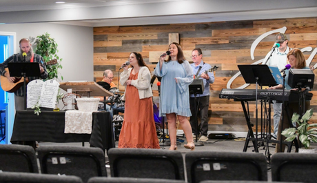 A band of people singing on stage at church. A piano and guitar are visible.