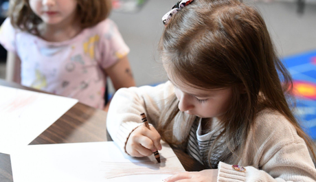 A teacher smiles at children seated around a table in a classroom.