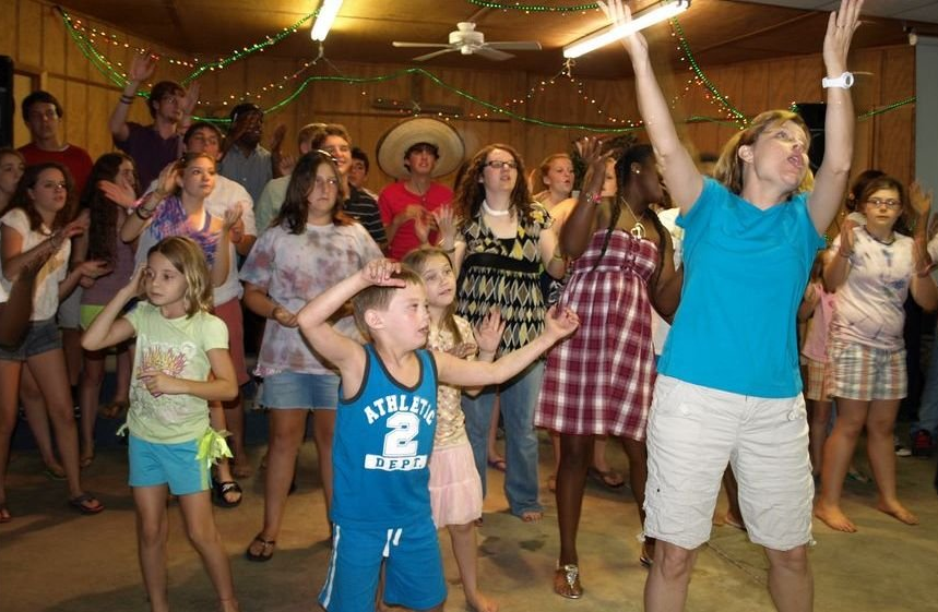 People dancing at a festive indoor summer camp with string lights and colorful decorations