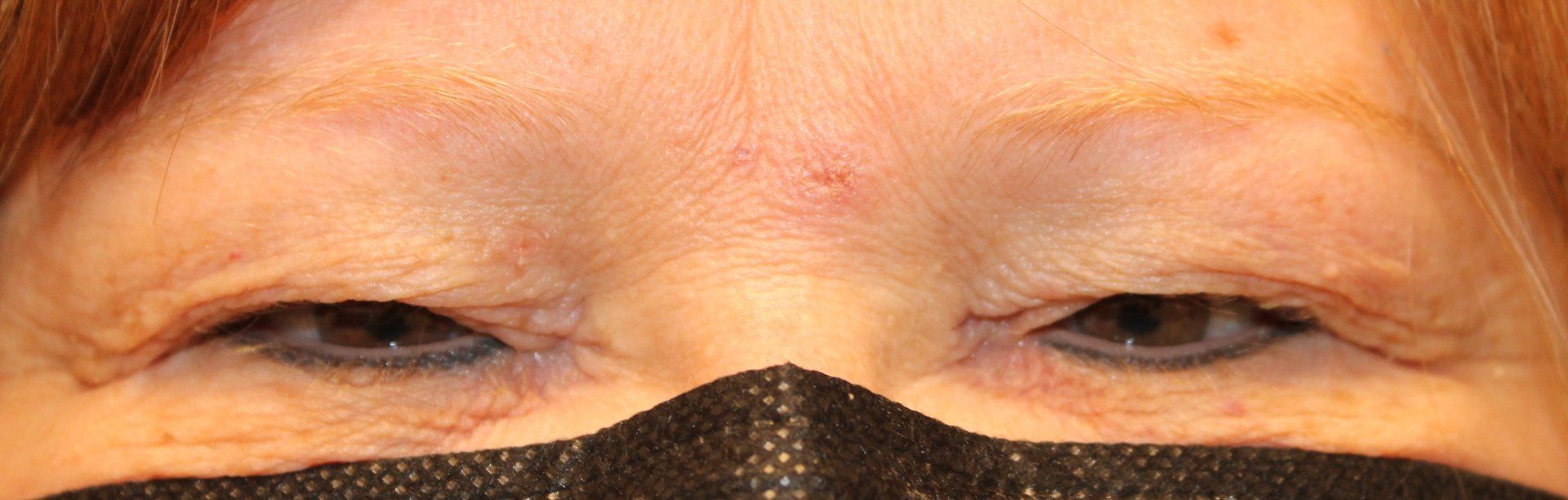 Close-up of eyes above a black face covering, looking slightly closed