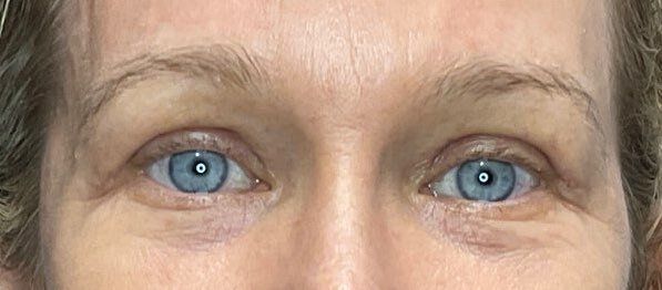 Close-up of blue eyes and eyebrows on a neutral face.