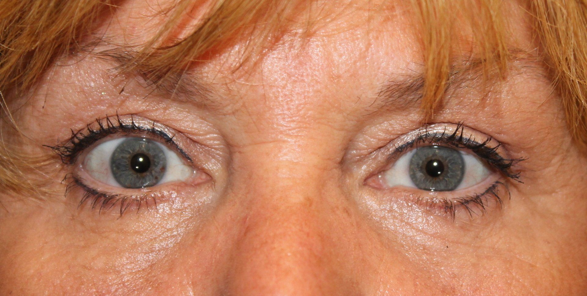 Close-up of blue eyes with light makeup and auburn bangs.