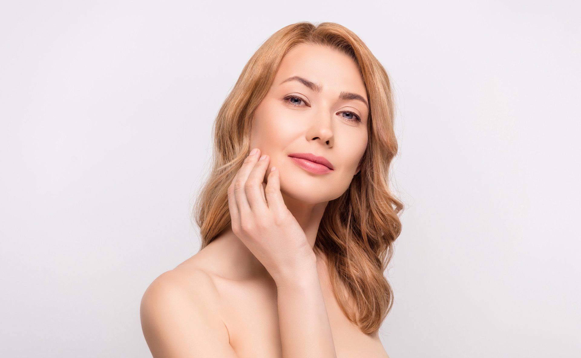 A woman is touching her face with her hand and smiling.