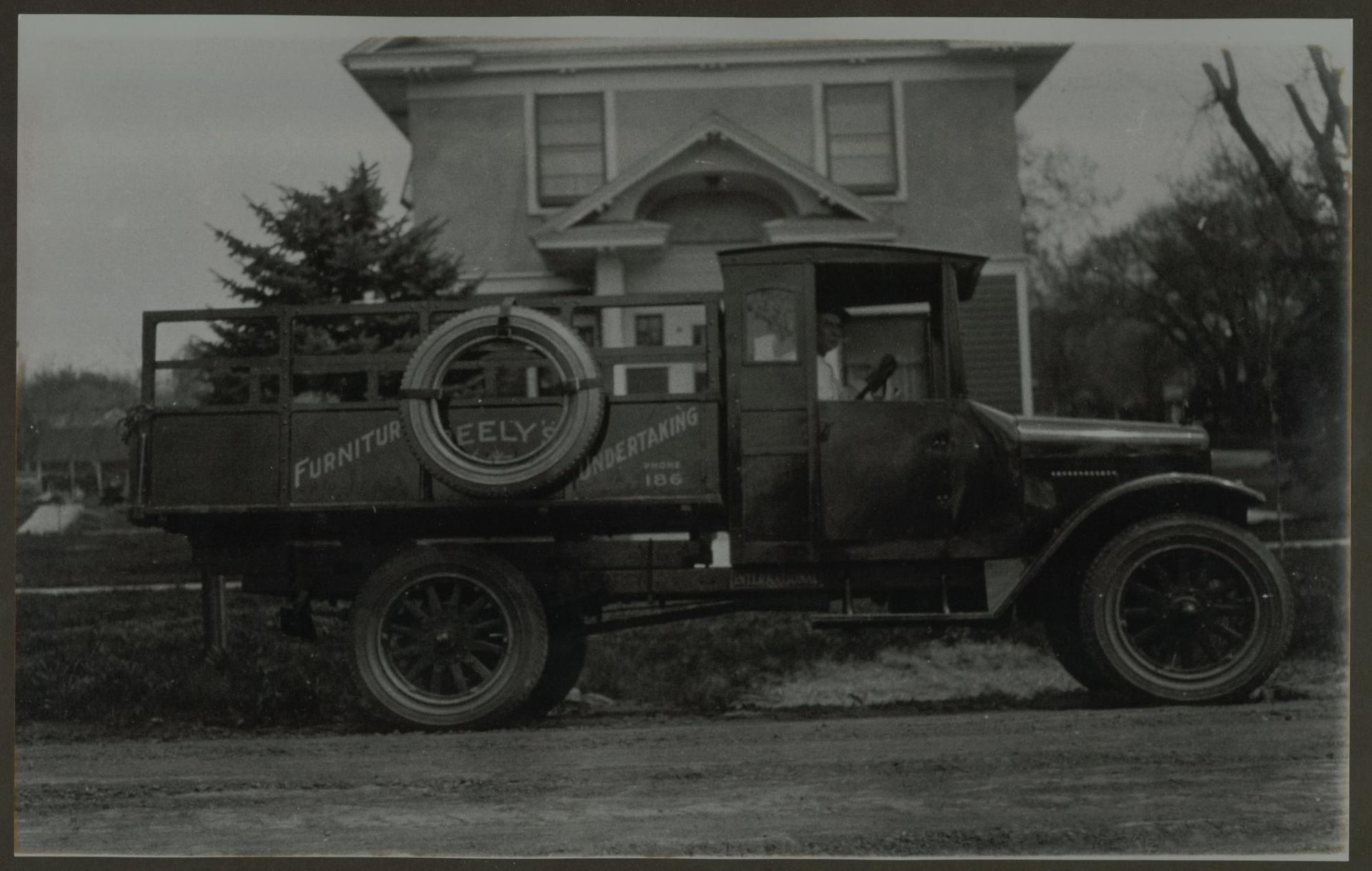 Vintage black pickup truck parked in front of a house, with a circular sign on its side.