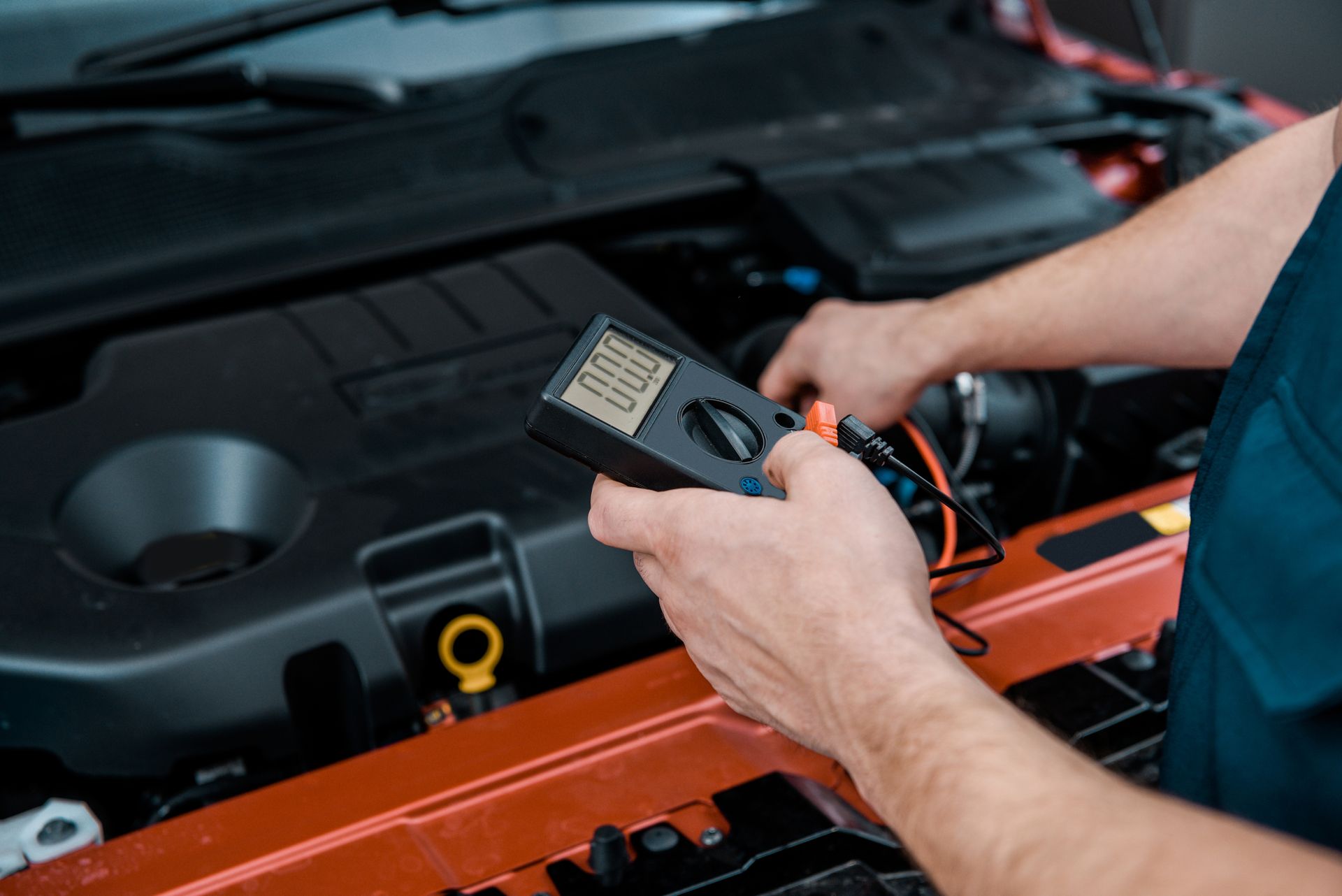 A man is holding a multimeter in front of a car engine.