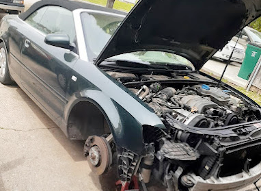 A convertible car with the hood up and a broken wheel.