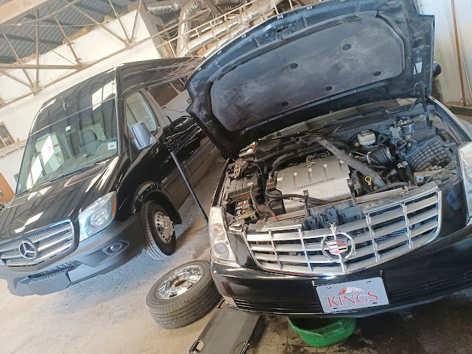 Two cars are parked next to each other in a garage with the hoods open.