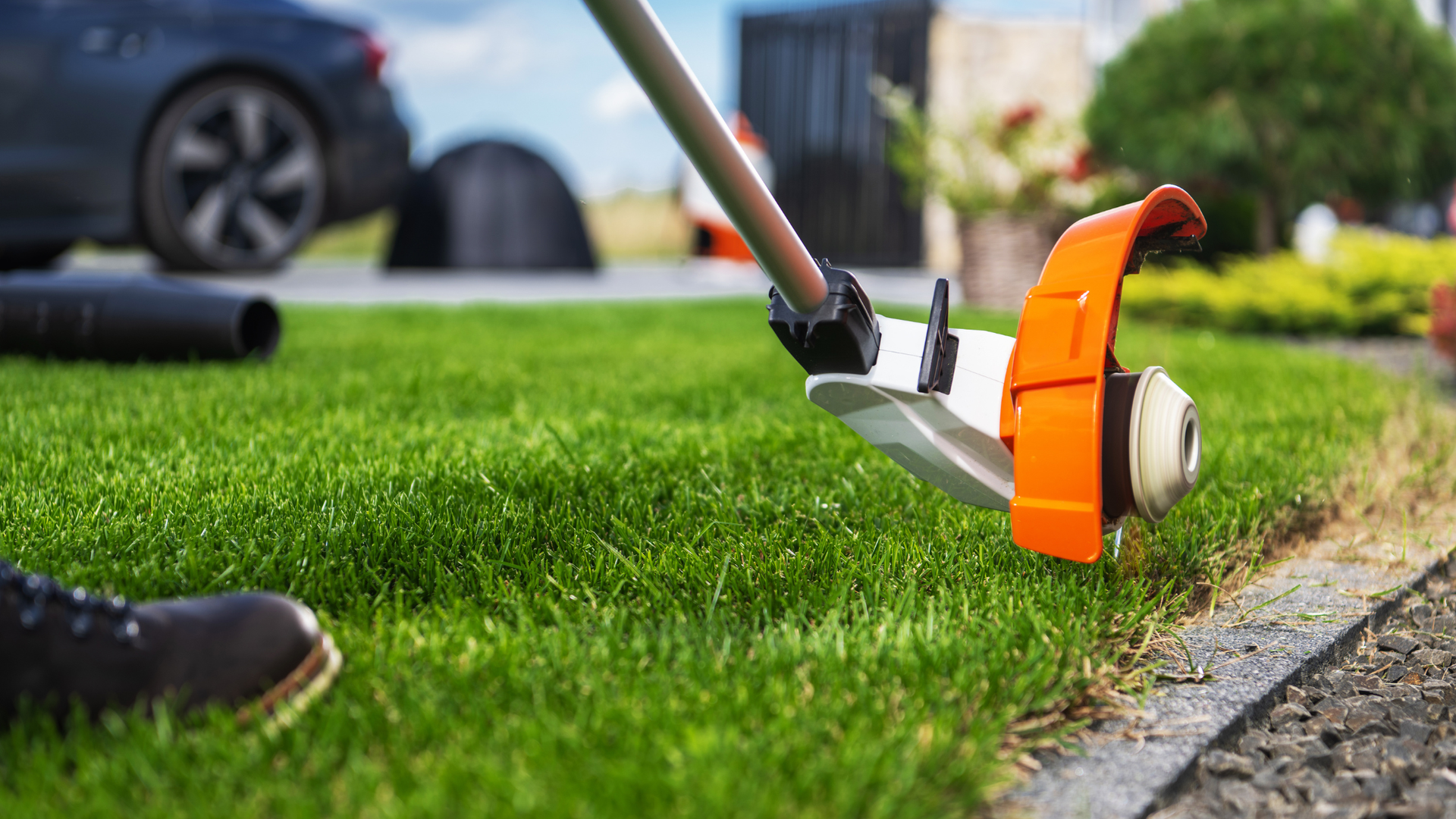 A close-up view of an orange and white string trimmer being used to edge a lawn next to a stone walkway.