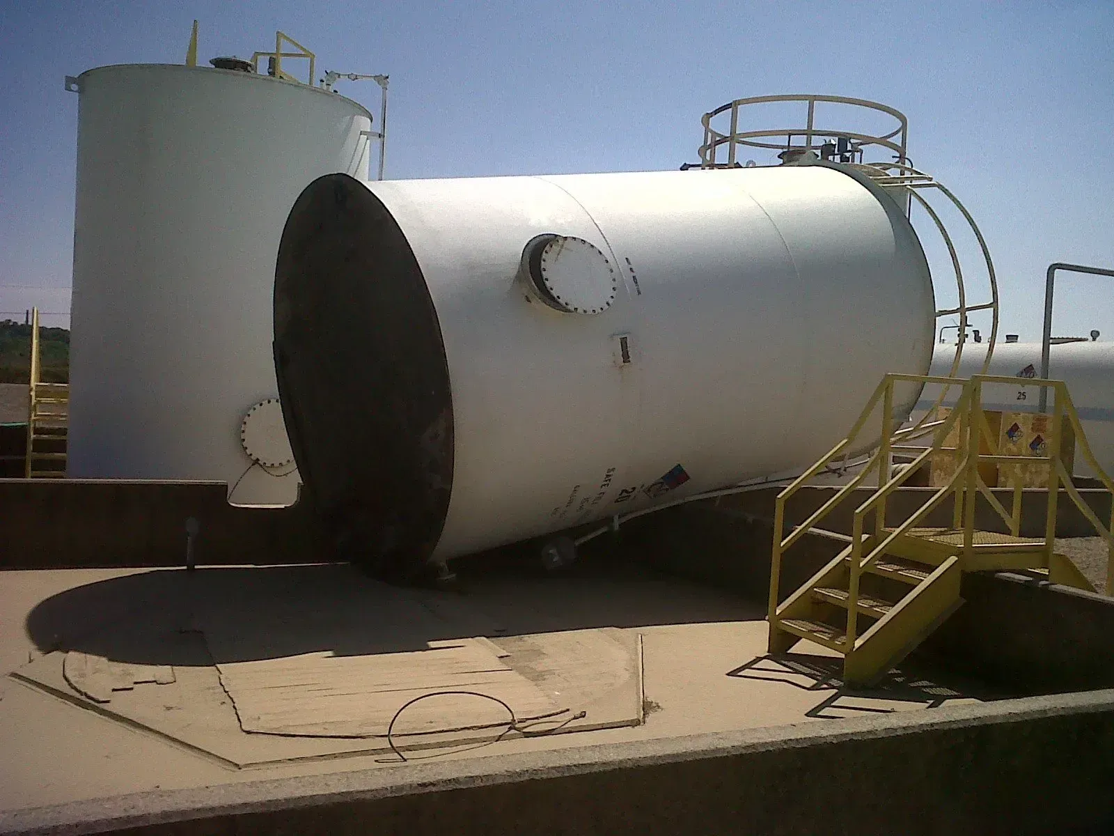 Overturned white storage tank with stairs, another tank in the background, set outdoors.