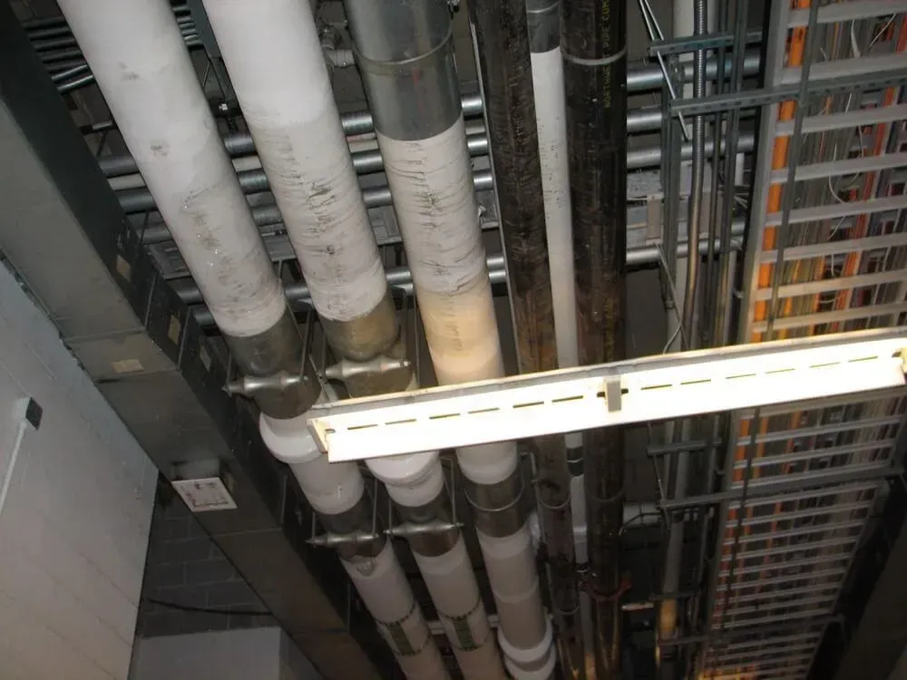 Pipes and cable trays running across a ceiling, with white insulation on some pipes.