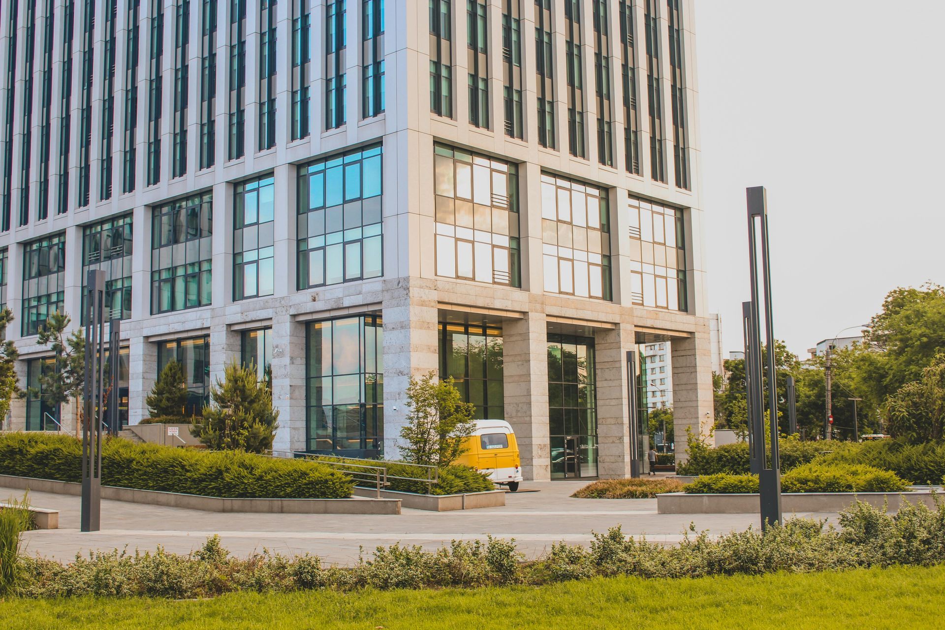 Modern office building with glass windows, yellow van parked in front.