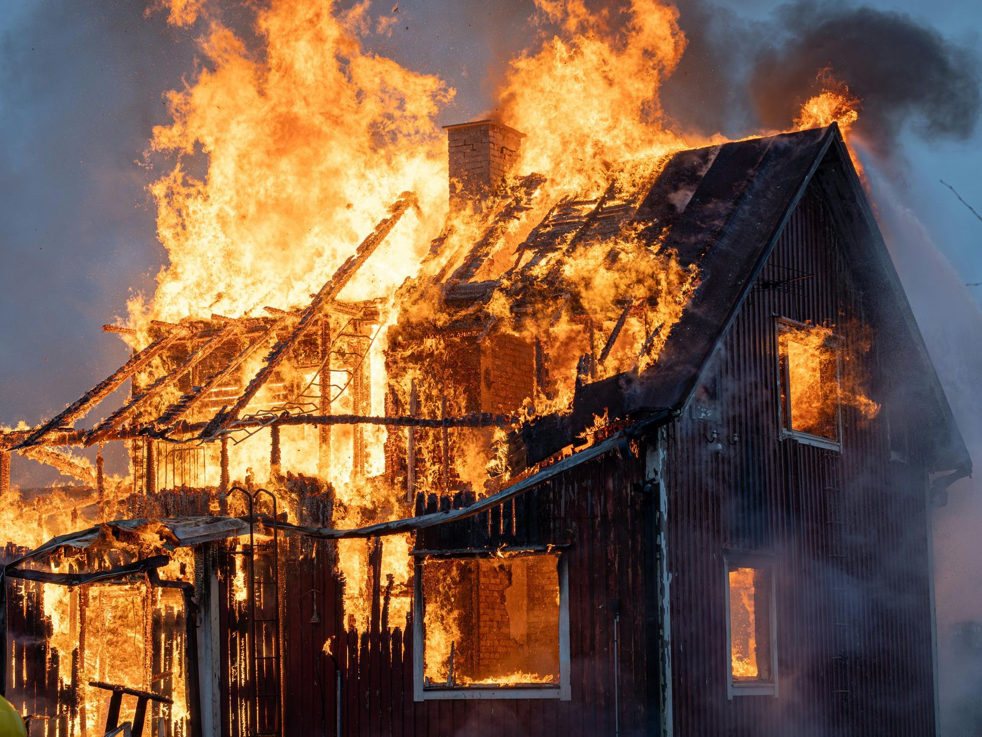 Burning wooden house; flames engulf roof and windows, smoke billowing.