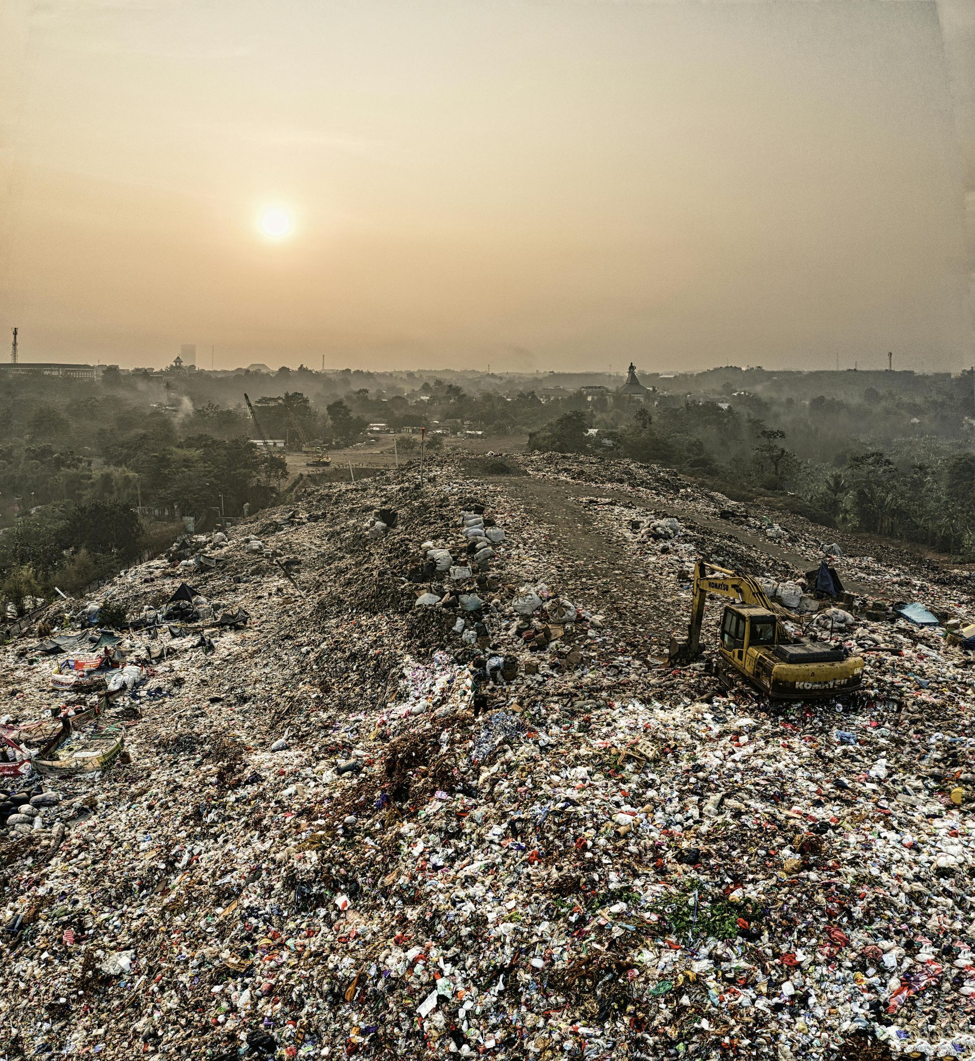 A large landfill with a bulldozer, under a hazy, sunlit sky.