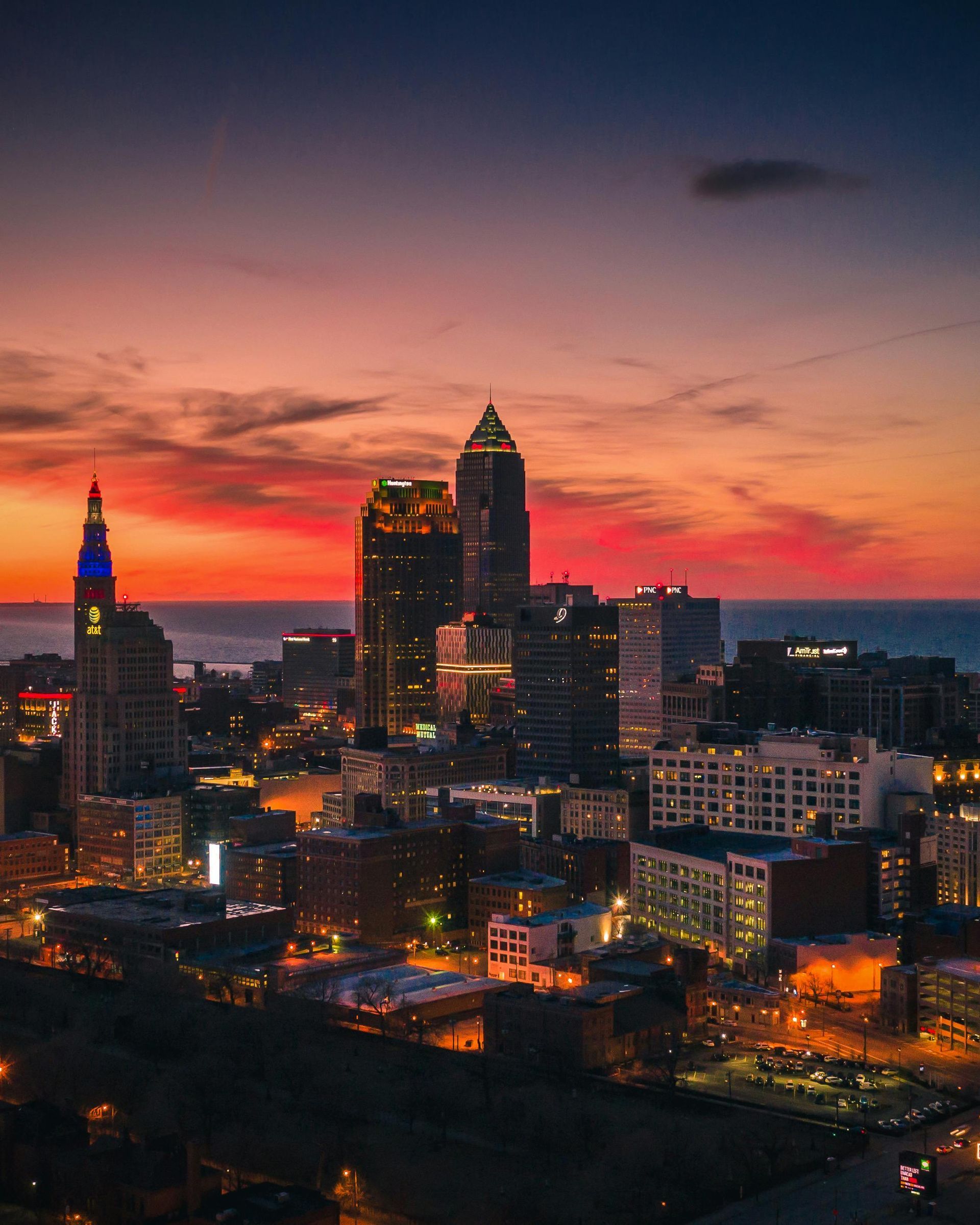Cleveland skyline at sunset, orange and blue sky, city lights, illuminated buildings.