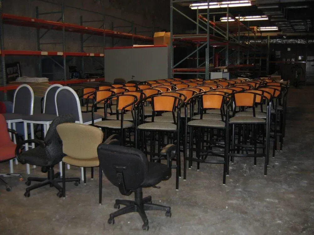 Chairs of various styles, including office and bar stools, arranged inside a warehouse.