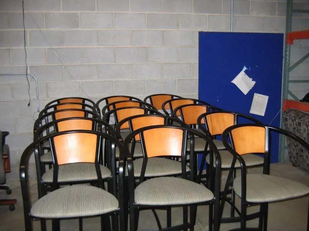 Row of chairs with light-colored seats and backs, black frames, against a brick wall. A blue board is also present.