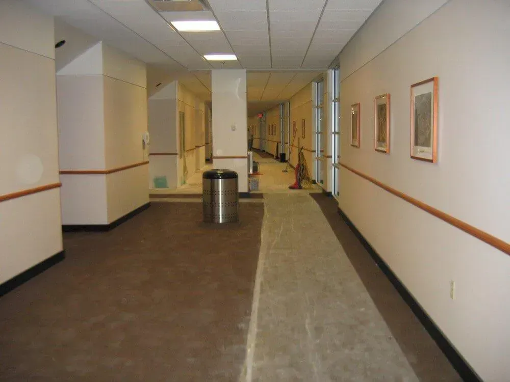 Hallway with beige walls, brown floor, and a silver trash can. Three framed pictures hang on the right wall.