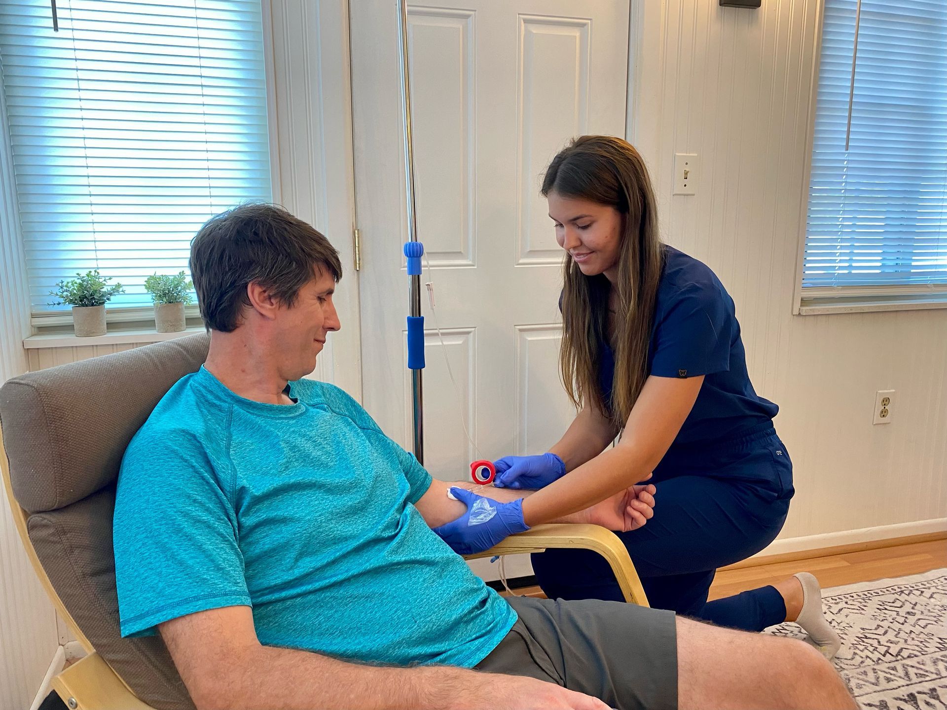 A woman is kneeling next to a man in a chair who is getting an iv.