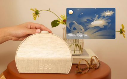 Round wooden tissue box on a desk beside glasses, with a blue floral card and dried flowers in the background