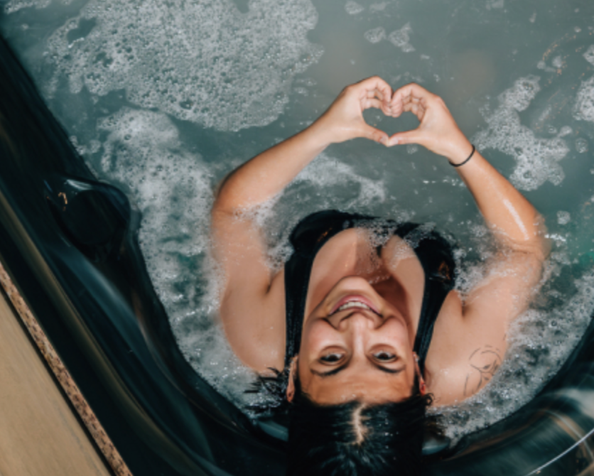 Woman floating on her back in water, smiling and making a heart shape with her hands.