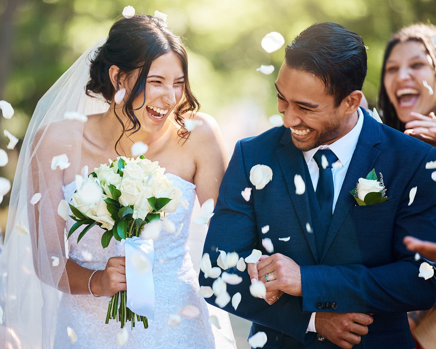 Bride and groom laughing as white petals fall during an outdoor wedding ceremony
