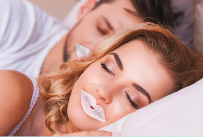 Two sleeping people in white bedding, one with a white lip strip in the foreground.