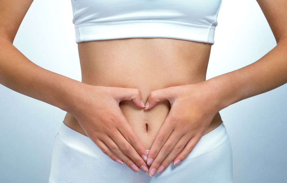 A woman is making a heart shape with her hands on her stomach