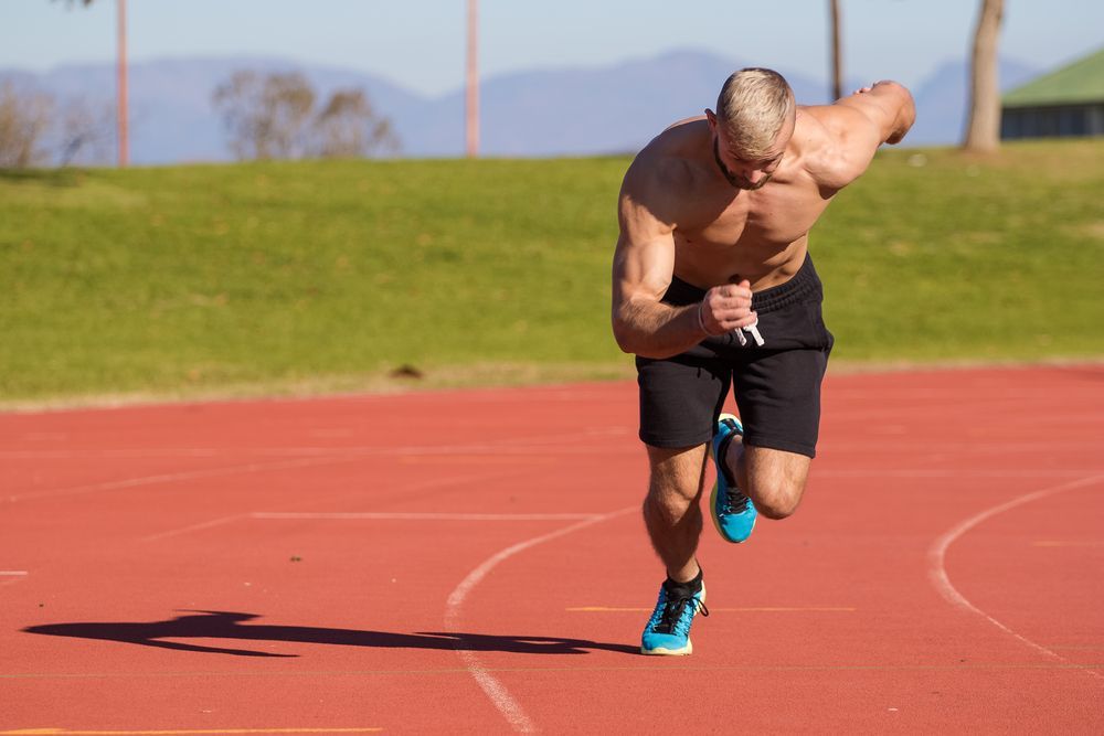 A shirtless man is running on a track.