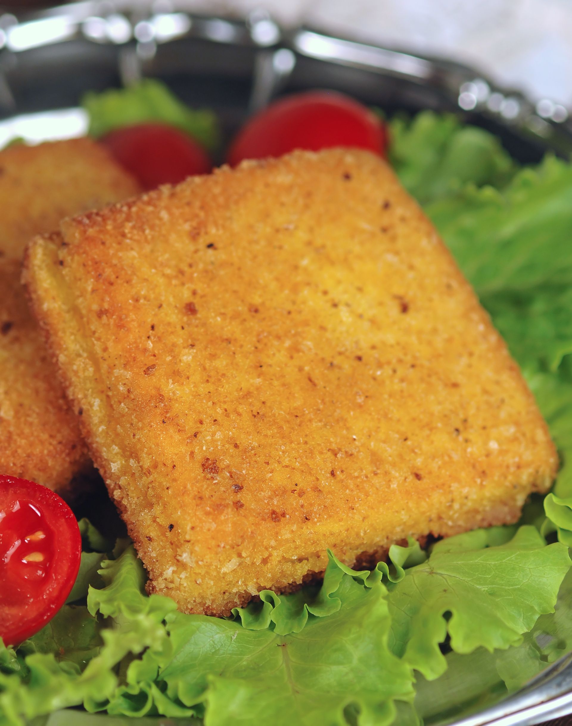 Formaggio quadrato dorato fritto su lattuga, con guarnizione di pomodoro.