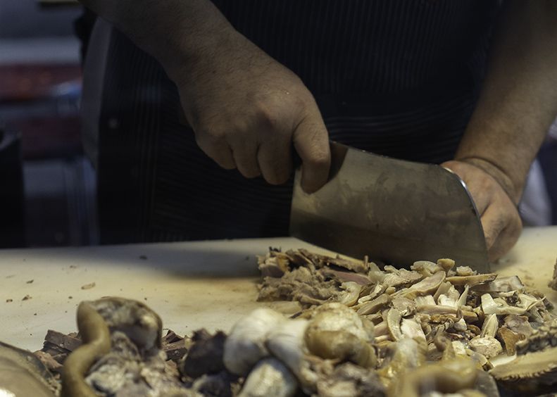 Macellaio che taglia la carne con una grande mannaia su un tagliere bianco.