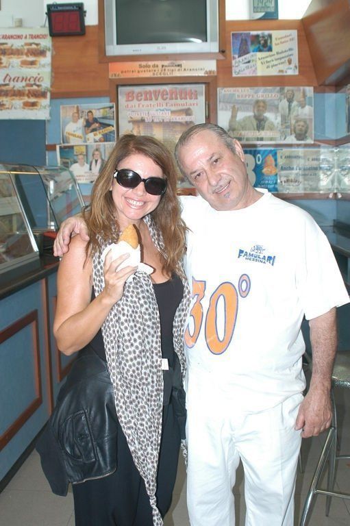 Una donna con occhiali da sole e un uomo con camicia bianca posano insieme. Sorridono all'interno di una panetteria.