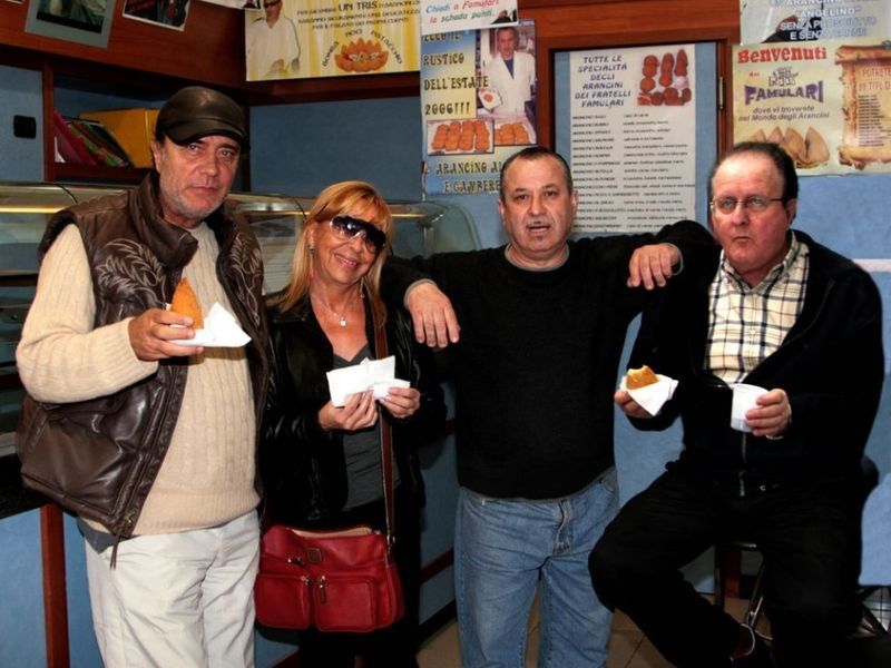 Quattro persone che mangiano, probabilmente in un negozio di alimentari. Tengono dei pasticcini e una è appoggiata al bancone.