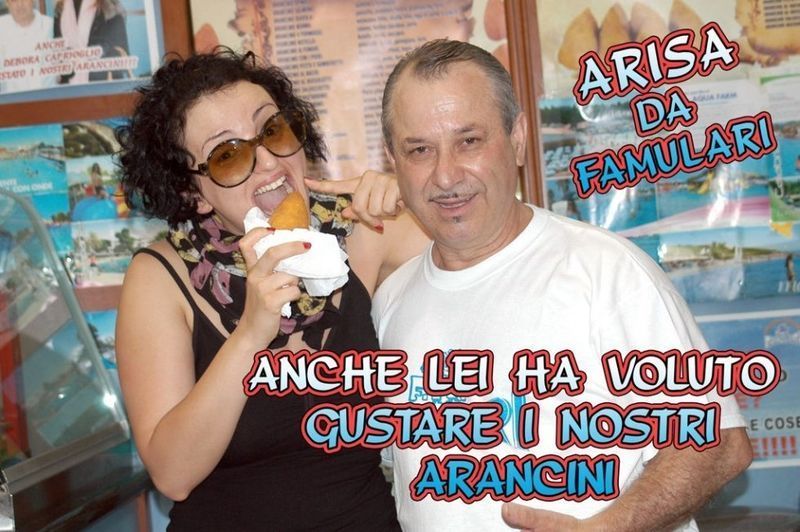 Donna che mangia arancini con un uomo; sullo sfondo vetrina; la scritta recita 