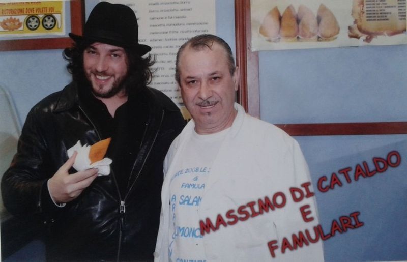 Un uomo con un cappello tiene in mano del cibo accanto a un uomo con la scritta 