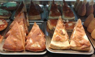 Esposizione di prodotti da forno, tra cui pasticcini triangolari e torte rotonde.