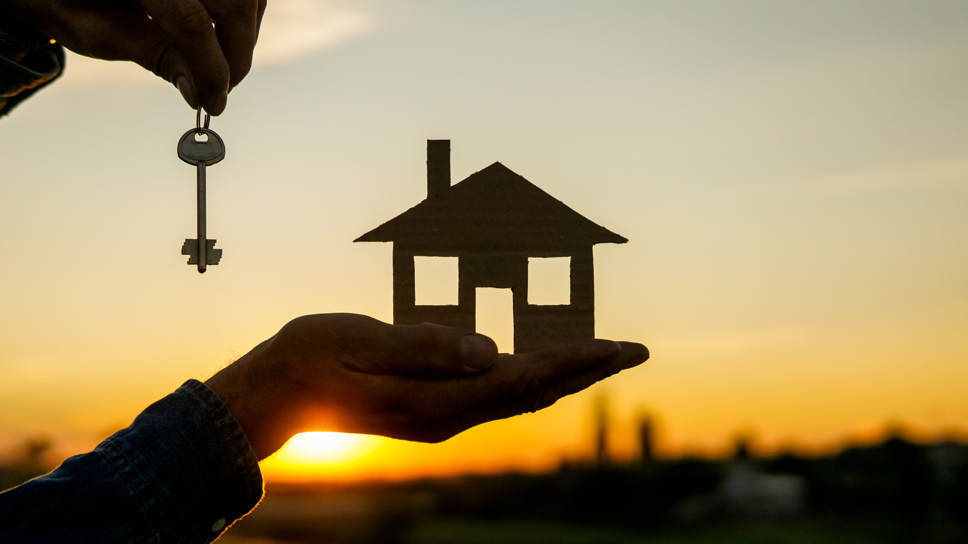 A person is holding a house and keys in their hand.