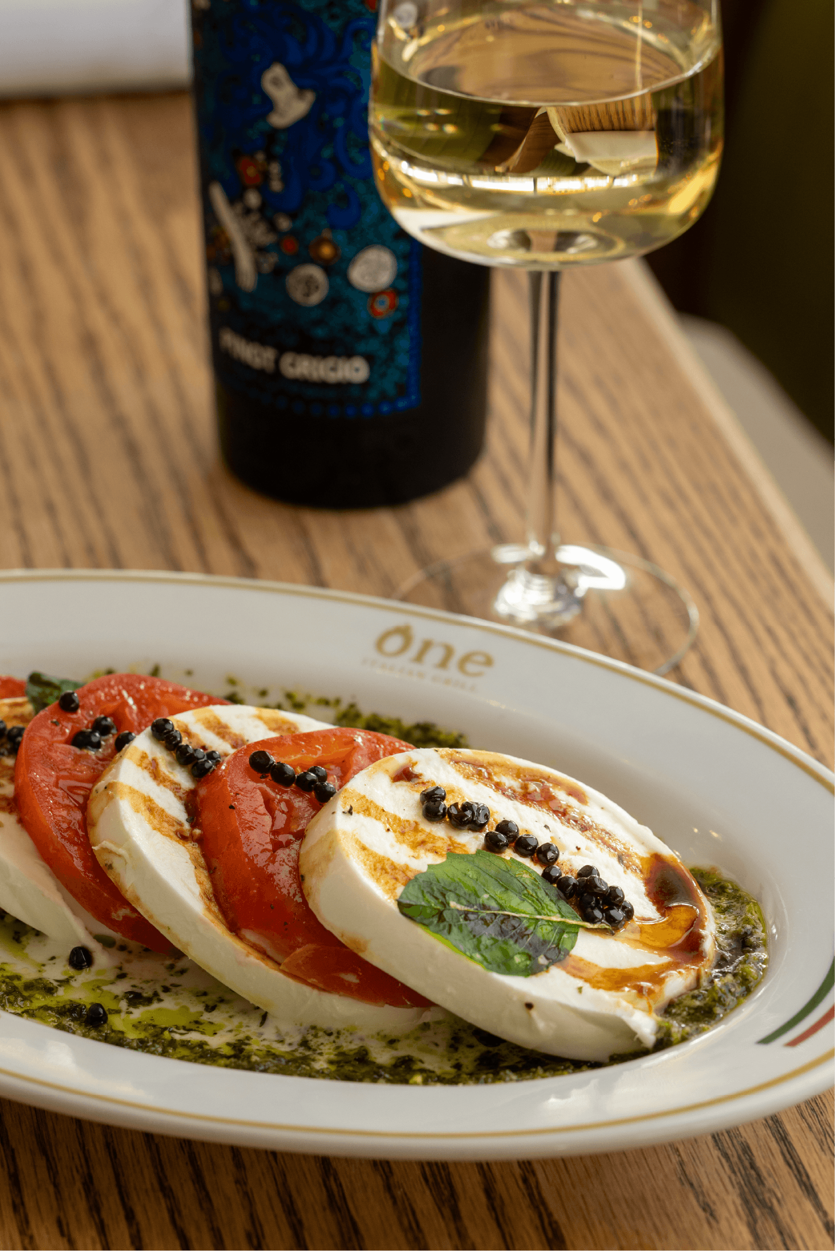 Several dishes in brass pans on a table with a wine bottle, and two rolled napkins.
