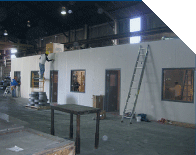 Interior of an unfinished building with white walls, windows, and a ladder on the right.