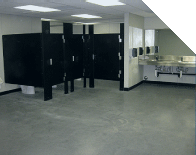 Public restroom with black stall doors, gray floor, and a row of sinks under bright fluorescent lights