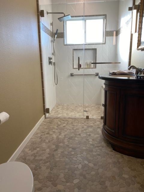 Bathroom with shower, window, wall-mounted grab bar, and a dark wood vanity.