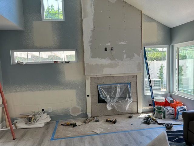 Living room under renovation with fireplace, painted walls, large windows, and tools on the floor